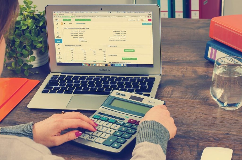 A woman providing bookkeeping services at a desk with a laptop and calculator.